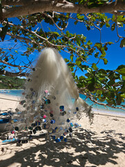 Fishing net dries on tree on beautiful white sand beach on sunny day near turquoise tropical wave sea. philippines islands. vertical