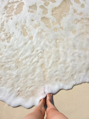 young woman legs and feet staying on beautiful white sand beach on sunny day near turquoise tropical wave sea. philippines islands. vertical