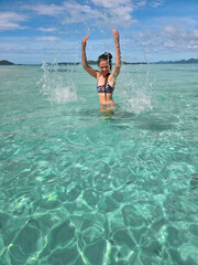 happy young woman in turquoise wave sea in philippines islands on sunny day. asia vocation. vertical