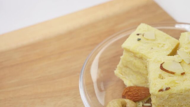 Patisa or Soan Papdi is a popular Indian cube shape flakey and crispy dessert. Served with almonds and pistachio in a plate over white background. Copy space and selective focus