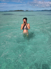 happy young woman in turquoise wave sea in philippines islands on sunny day. asia vocation. vertical