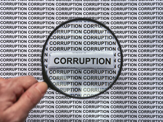 A person with a magnifying glass in his hand magnifying the words Corruption on a newspaper print background. Close up.