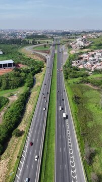 Filmagem a&eacute;rea da Rodovia Ayrton Senna com fluxo constante de ve&iacute;culos, destacando infraestrutura moderna e integra&ccedil;&atilde;o com &aacute;reas verdes.
