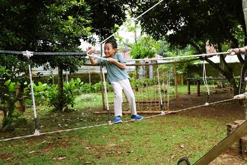 A young child balancing carefully on a rope game in an outdoor playground. Natural surroundings emphasize active play, coordination training, and healthy growth through outdoor recreation.