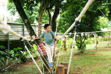 Active child crossing a rope bridge in a natural play area, encouraging confidence, physical development, and connection with the environment.