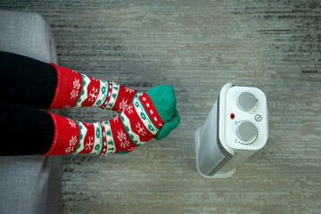 top view of crossed feet and an electric heater (fan heater) as a symbol of cold and energy poverty during winter