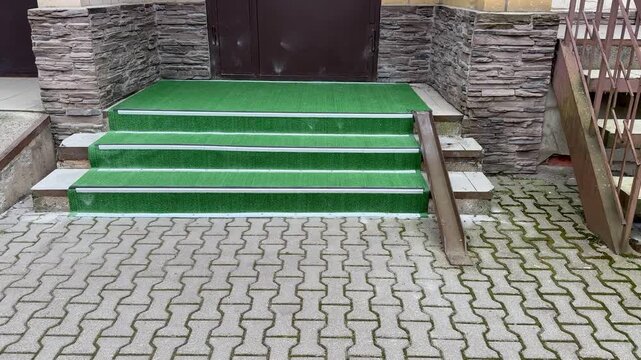 Green Turf Covered Outdoor Steps At Stone Entrance With Metal Handrail, Interlocking Pavers And Worn Edges, Subtle Moss Along Joints, Maintenance Access To Rooftop Service Area, Muted