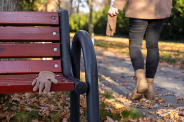 A single beige glove sits abandoned on a weathered wooden park bench, surrounded by vibrant fallen...