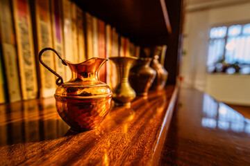 Close up photograph of small copper and bronze Turkish coffee pots displayed on a bookshelf. The...