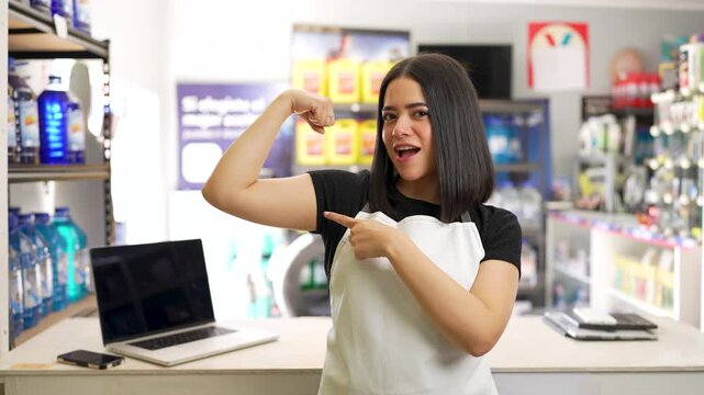 Confident young saleswoman flexing her biceps and smiling while working at a hardware store