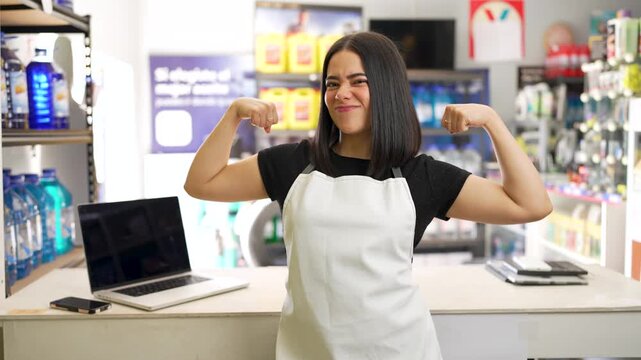 Confident young hardware store employee smiling, pointing at camera, and showing her strength
