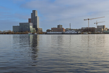 View of the developing Sluisbuurt district in Amsterdam. Skyline with new high-rise buildings, construction cranes, and a ship on the water.