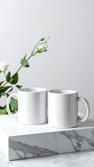 Two plain white mugs on a marble platform, with a sprig of white flowers