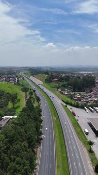 Vista a&eacute;rea vertical da Rodovia Ayrton Senna, mostrando a pista duplicada, o fluxo de ve&iacute;culos e a import&acirc;ncia da via para a mobilidade regional em S&atilde;o Paulo.
