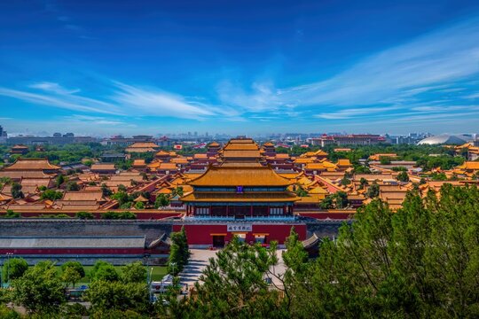 Aerial view of the Forbidden City in Beijing, showcasing the iconic central axis of ancient Chinese architecture, surrounded by green landscapes and modern city skyline.