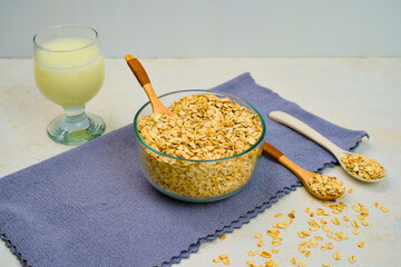 A healthy bowl of rolled oats resting beside a glass of oat milk and wooden spoons set upon a textured purple napkin for a nutritious breakfast concept.
