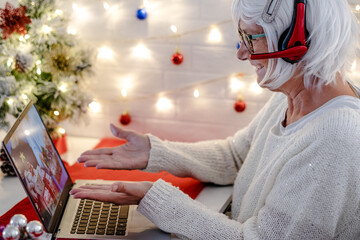 Happy white haired senior woman using laptop in video call with distant family celebrating Christmas