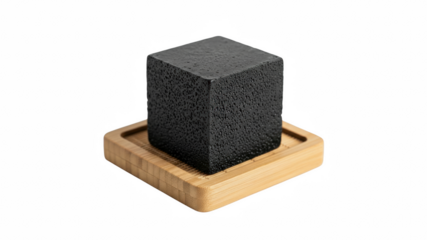 Rectangular block of porous black charcoal soap with moisture droplets resting on a small square bamboo drainage dish on transparent background
