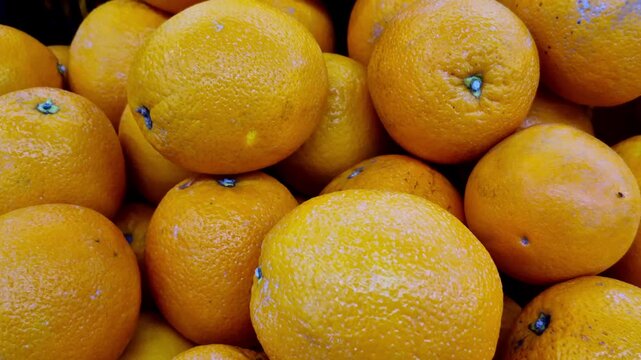 A close-up of fresh oranges piled together at a market stall, showing bright orange peels with dimpled texture and natural surface variations under soft daylight.