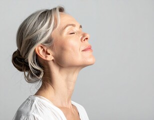 Mature woman with gray hair in a bun, eyes closed, enjoying a moment of peace and tranquility