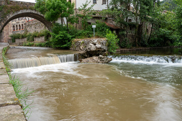 A bridge over a river with a sign on it in village of Potes. The water is brown and the bridge is old