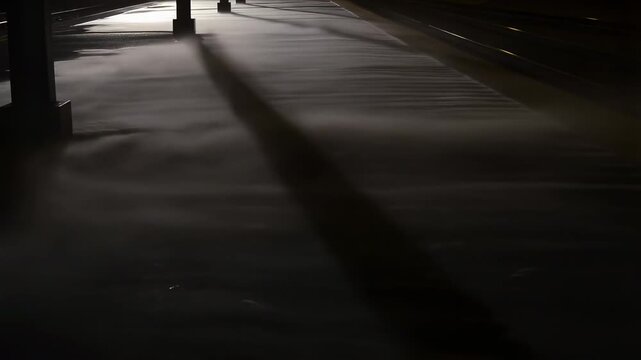 Mysterious shadows cast on dark railway platform as train passes at night