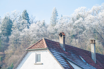 L&auml;ndliches Haus mit Kr&uuml;ppelwalmdach und zwei Schornsteinen mit Dach und Lichterkette am Giebel vor frostbedeckten B&auml;umen und blauem Himmel in Neckartenzlingen