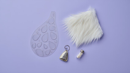 Artistic Still Life Composition Featuring a Teardrop Shaped Template, Faux Fur Piece, Small Bell, and Tiny Bottle on a Light Purple Background for Crafts