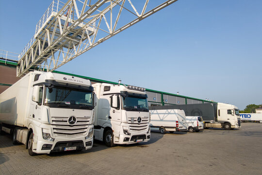 Warsaw, Poland &mdash; June 1, 2025: A line of white delivery vans and a Mercedes-Benz Actros truck parked at a logistics center loading dock under a clear sky during daytime