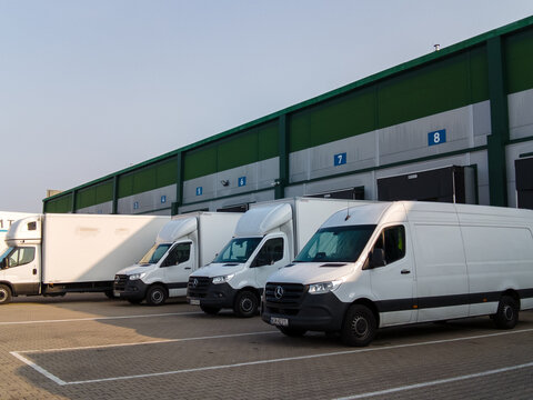 Warsaw, Poland &mdash; June 1, 2025: A line of white delivery vans and a Mercedes-Benz Actros truck parked at a logistics center loading dock under a clear sky during daytime