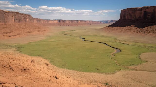 Vast Green Valley Surrounded by Red Rock Formations Under a Bright Blue Sky