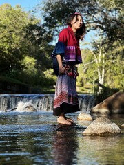Beautiful Asian woman in modern Hmong traditional dress standing by a waterfall.