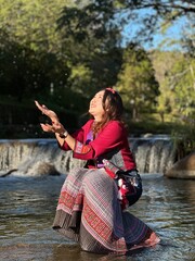 Smiling traveler enjoying nature in traditional hill tribe attire at a waterfall.