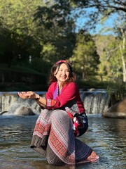 Smiling traveler enjoying nature in traditional hill tribe attire at a waterfall.