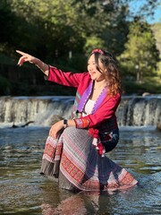Smiling traveler enjoying nature in traditional hill tribe attire at a waterfall.