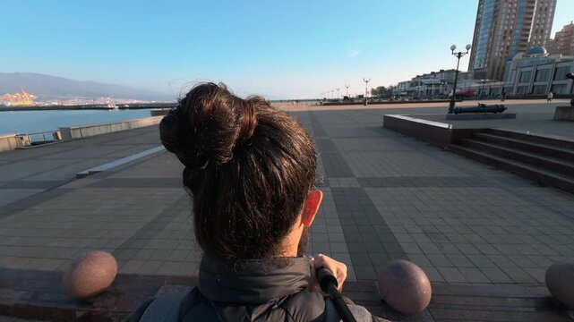 A walk along the paved embankment of Novorossiysk. Rear view. Bodycam footage. Back of a man's head with long hair. Golden hour. Wide angle. Atmospheric B-roll