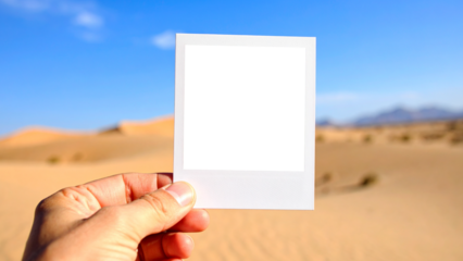 Creative concept of travel and memories. Man's hand holding an instant picture of a desert landscape against a blurred background of the same scene. Focus on the sharp photo and nostalgia.