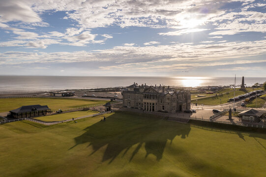 Aerial view of the iconic Royal and Ancient Golf Club clubhouse casting long shadows across the lush green links, St Andrews, Scotland, United Kingdom.