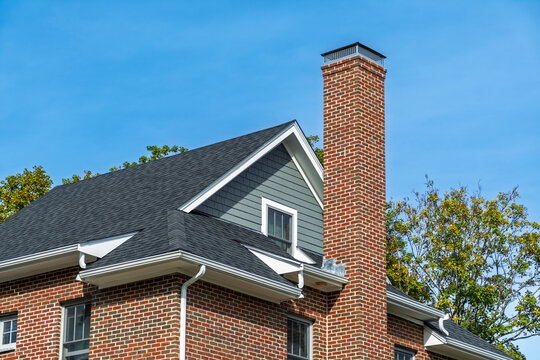 Classic brick chimney rising above a traditional residential house roof under blue sky in Boston, Massachusetts, USA
