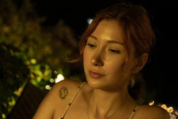 A portrait of a stunning young woman sitting at a cozy outdoor cafe table, drinking coffee during a warm summer evening. Soft ambient lighting, lifestyle photography, and a relaxed atmosphere.