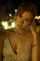 A portrait of a stunning young woman sitting at a cozy outdoor cafe table, drinking coffee during a warm summer evening. Soft ambient lighting, lifestyle photography, and a relaxed atmosphere.