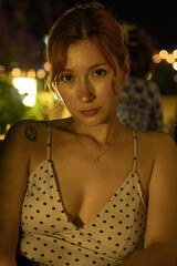 A portrait of a stunning young woman sitting at a cozy outdoor cafe table, drinking coffee during a warm summer evening. Soft ambient lighting, lifestyle photography, and a relaxed atmosphere.