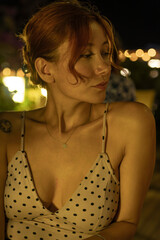 A portrait of a stunning young woman sitting at a cozy outdoor cafe table, drinking coffee during a warm summer evening. Soft ambient lighting, lifestyle photography, and a relaxed atmosphere.