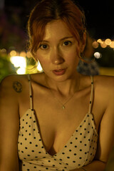 A portrait of a stunning young woman sitting at a cozy outdoor cafe table, drinking coffee during a warm summer evening. Soft ambient lighting, lifestyle photography, and a relaxed atmosphere.