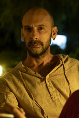 A portrait of a mature man sitting at a cozy outdoor cafe table during a warm summer evening, enjoying a cup of coffee. He looks relaxed and thoughtful in a modern urban lifestyle setting.