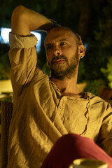 A portrait of a mature man sitting at a cozy outdoor cafe table during a warm summer evening, enjoying a cup of coffee. He looks relaxed and thoughtful in a modern urban lifestyle setting.