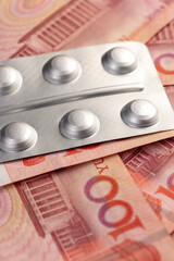 Chinese cash for a hundred yuan and pills in a packaged blister, medicines and red Chinese cash with a face value of 100 yuan are lying together.