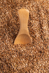 flax seeds for sowing in one wooden spoon, a large number of light brown flax seeds and a wooden spoon with seeds