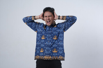 Indonesian PNS teacher in blue batik uniform showing frustration and burnout, covering ears while...