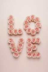 Word LOVE made of pink roses buds on pale pink background top view. Romantic, holiday, Valentine's day, wedding, birthday, Mother's day, day concept